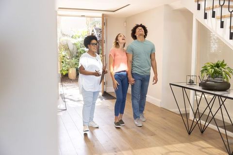 Real estate agent showing young couple modern sunlit foyer with staircase and courtyard