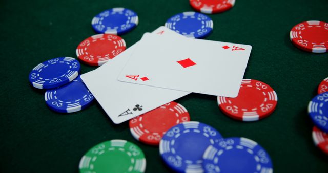 An arrangement of red, blue, and green poker chips scattered on a green casino table, with two aces (diamonds and clubs) prominently shown. Perfect for illustrating concepts of gambling, luck, strategy and casino gameplay. Suitable for use in articles, advertisements, or blogs on poker, casinos, or gaming strategies.