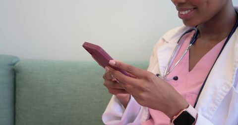 African female clinician using smartphone on clinic sofa for telehealth communication