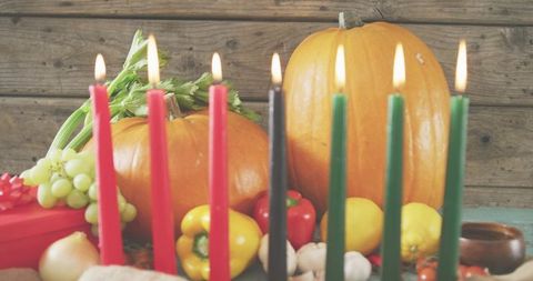Burning seven red black green candles with pumpkins and harvest produce on rustic wood table
