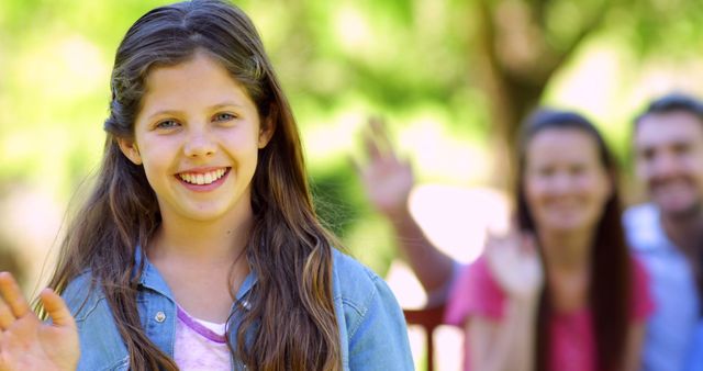 Smiling Girl Waving Outdoors with Family in Background - Download Free Stock Images Pikwizard.com