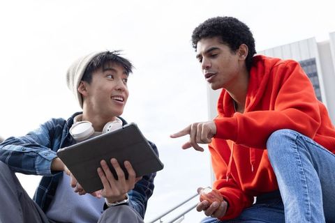 Diverse male students collaborating on tablet outdoors on campus steps, casual study