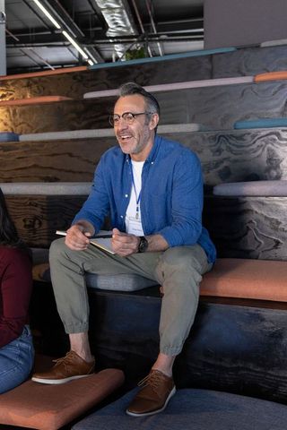 Middle-aged man smiling and taking notes during casual coworking meeting in modern office