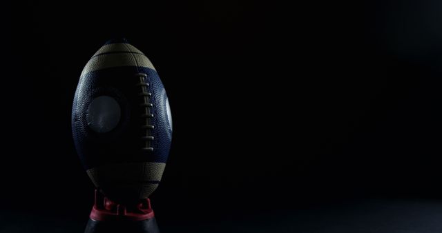 Football ball placed on a stand, highlighted with low light. Ideal for use in sports advertisements, football event promotions, and articles related to sports equipment. The dark background adds a dramatic and intense atmosphere suitable for contexts focusing on sports intensity and competition.