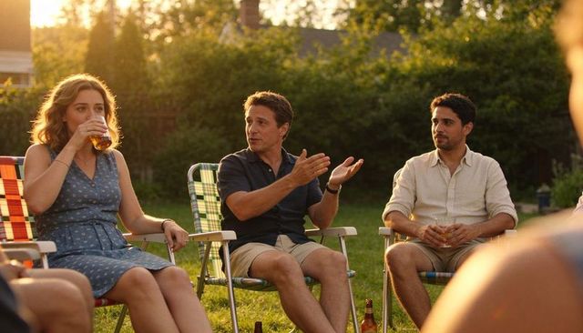 Friends chatting on suburban lawn during golden hour with cold drinks and lawn chairs