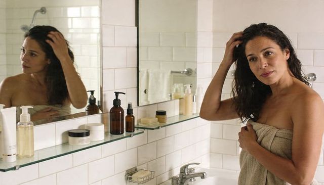 Woman wrapped in towel adjusting hair at bathroom sink reflecting quiet self-care routine