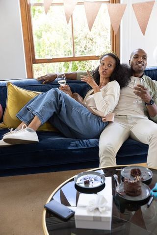 African american couple toasting on velvet sofa celebrating birthday at home with cake