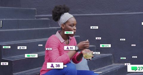 Young woman checking smartwatch while eating salad on urban steps with social media badges