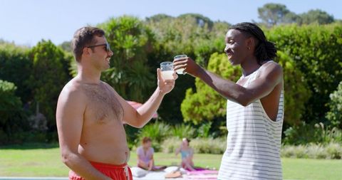 Male Friends Toasting Drinks by Backyard Pool on Sunny Day