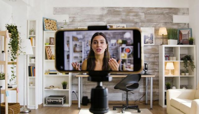 Recording vlogger in cozy home studio using smartphone on tripod for live content
