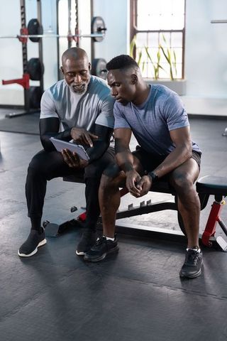 African american trainer coaching young male athlete using tablet in strength gym