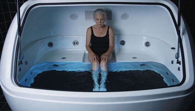 Senior woman sitting in hydrotherapy tub soaking feet under blue led jets for relaxation