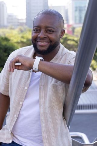 Smiling african american man leaning on rooftop pole wearing white smartwatch portrait