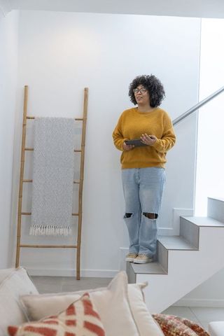Young woman using tablet on modern minimalist stair landing wearing mustard sweater