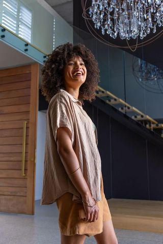 African american woman smiling in modern foyer admiring crystal chandelier and glass staircase