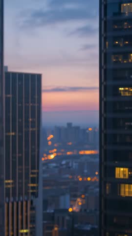 Vertical dusk city video revealing skyline through skyscraper gap with glowing office lights