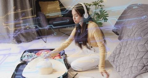 Young woman packing suitcase wearing headphones with futuristic travel data overlay