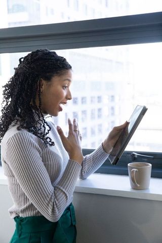 Smiling african american woman holding tablet during video call at office window