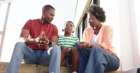 African american parents listening and talking with son on front steps in bright sunlight