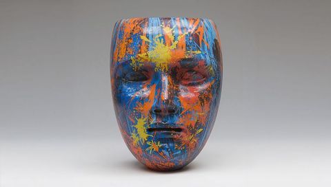 Color-splattered ceramic face mask sculpture glossy blue base orange yellow accents