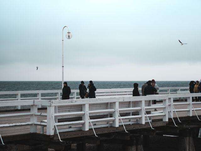 People Strolling on a Pier by the Ocean Under Cloudy Sky - Download Free Stock Photos Pikwizard.com