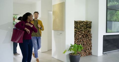 Diverse friends entering modern home wearing burgundy sweater carrying maroon tote