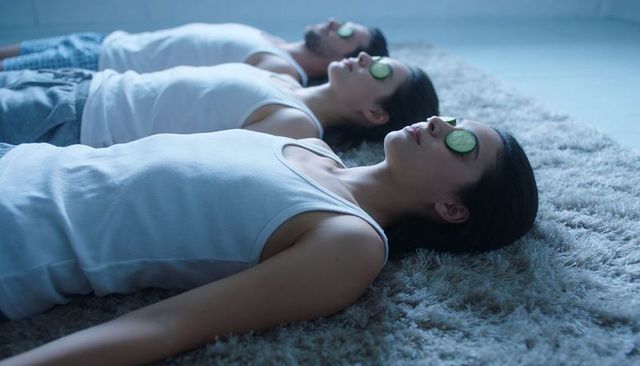 Three friends relaxing with cucumber eye slices on gray shag rug at home spa