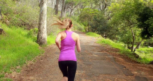A young Caucasian woman is jogging on a path through a lush green park, with copy space. Her active lifestyle is captured as she exercises outdoors, promoting health and fitness.
