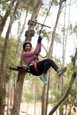 Young woman enjoying zipline adventure in forest ropes course