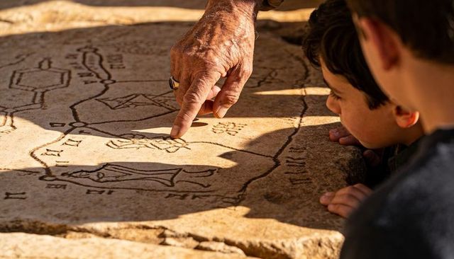 Senior pointing at ancient stone map guiding curious child at open-air ruins