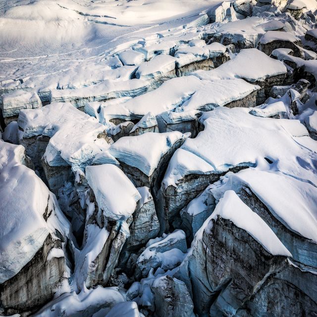 Dramatic aerial perspectives showcasing rugged snow-covered mountain glacier with striking ice crevasses. Highlights harsh natural winter landscapes, suitable for climate change presentations, nature documentaries, travel articles or educational materials on geological formations.