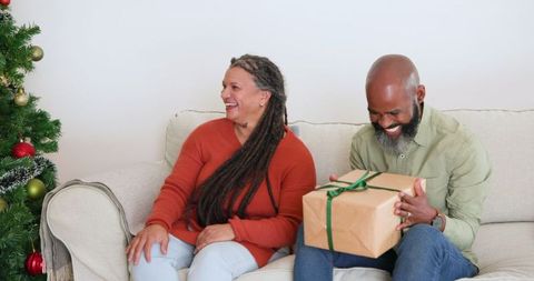 Joyful elderly couple exchanging christmas present in cozy living room