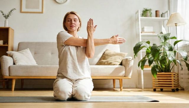 Kneeling woman stretching arms on yoga mat in sunlit minimalist living room for wellness