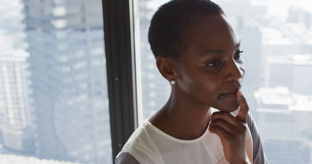 Elegant African American businesswoman is pondering while looking out window in modern high-rise office. Perfect for use in corporate, diversity, leadership or career development materials.