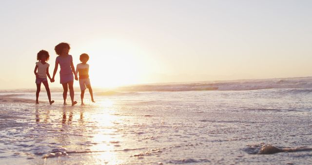 African american mother son and daughter having fun walking together during sunset on the beach. family travel vacation leisure concept