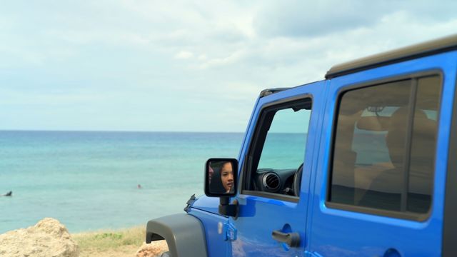 Couple reflecting in rear-view mirror while enjoying their time inside a blue car parked on a beach near the ocean. Suitable for travel and adventure campaigns, promoting beach vacations, summer holidays, car and auto lifestyle content, and relationship themes.