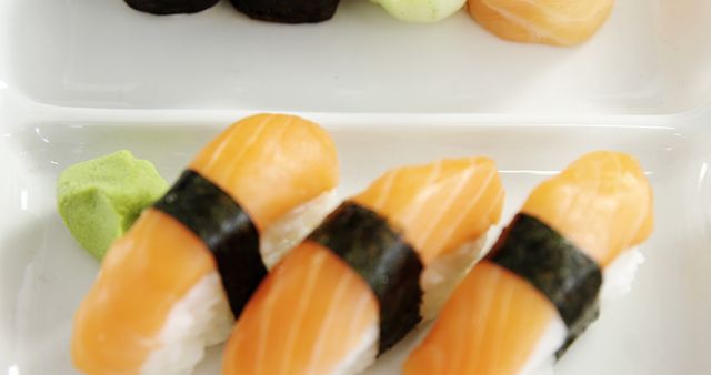 Fresh salmon nigiri served with wasabi on a sleek white plate. Ideal for illustrating articles about Japanese cuisine, seafood recipes, or gourmet dining. Useful for food blogs, restaurant menus, and culinary presentations.