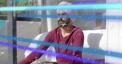 Indian man wearing pale-pink turban gazing through glass door with light streak overlays