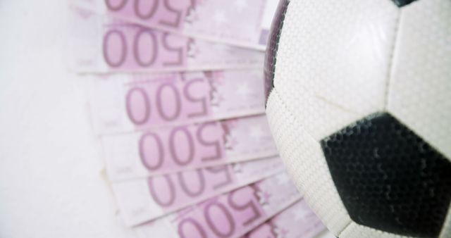A soccer ball is prominently featured against a background of Euro currency notes, with copy space. It suggests a concept of sports financing or the economic aspects of soccer.