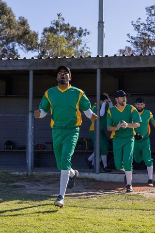 Baseball team celebrating victory running out of dugout in green and yellow uniforms