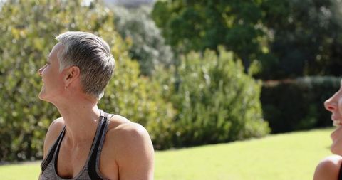 Mature woman laughing and chatting on sunny lawn during outdoor fitness and wellness meetup