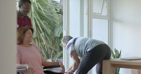 Senior Caregiver Offering Assistance to Smiling Elderly Woman in Wheelchair