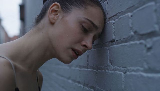 Distressed woman leaning against painted brick wall in urban alleyway moody closeup