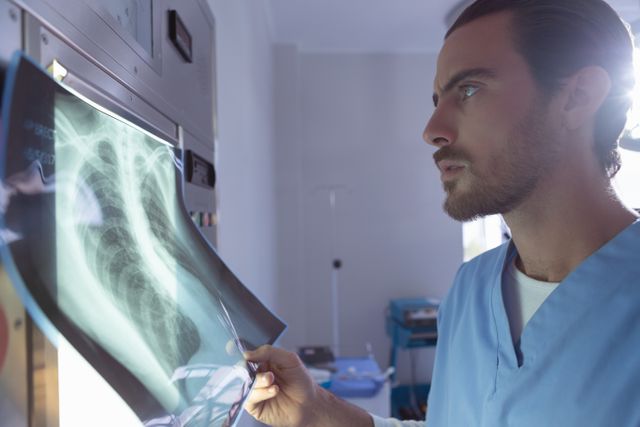 Male surgeon closely examining a chest x-ray in a hospital operation room. Ideal for use in medical articles, healthcare websites, and educational materials about radiology, diagnosis, and patient care.