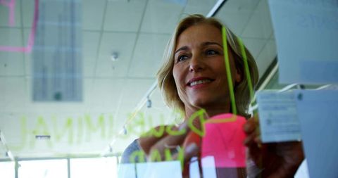 Businesswoman organizing neon sticky notes on glass board during modern creative brainstorming