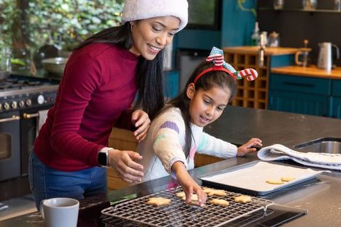 Asian mother guiding daughter placing star cookies on cooling rack in cozy festive teal kitchen