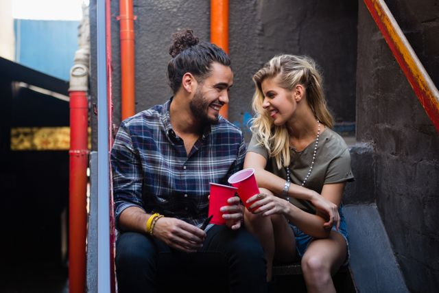 Happy couple interacting while having drink on staircase of bar