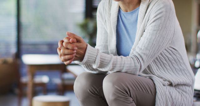 An elderly person sits indoors, deep in thought, wearing a cozy white sweater. Use this image for articles on aging, mental health, senior living, reflective moments, or home comfort.