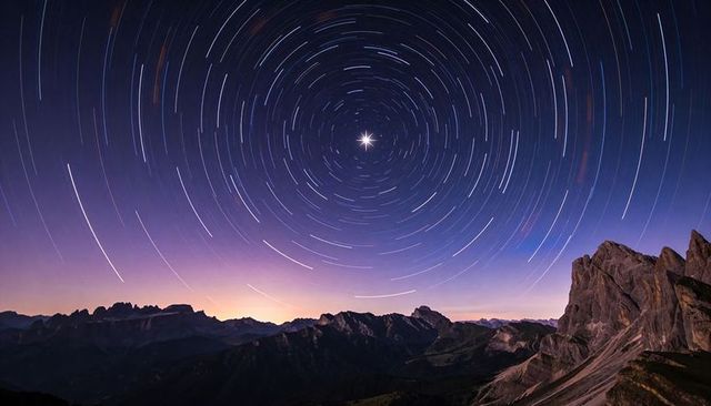 Rotating polar star trails circling over alpine ridge at twilight with dramatic rock cliffs