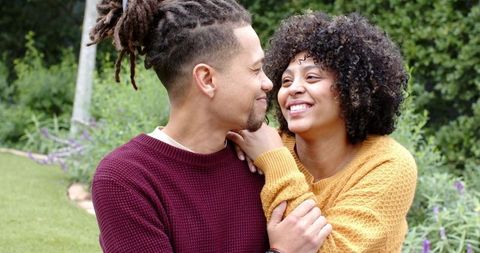 Young couple sharing warm embrace in garden wearing cozy mustard and burgundy knits